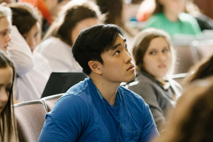 A male student in a classroom looks upward in thought.